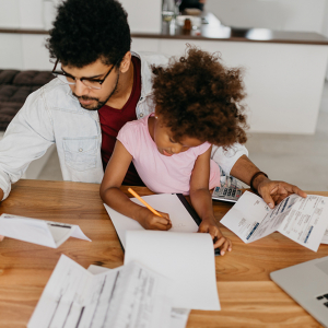 Father reading financial documents while his young daughter draws a picture.
