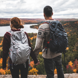 Un couple en randonnée sur une colline rocheuse admire les couleurs automnales de la forêt en contrebas.