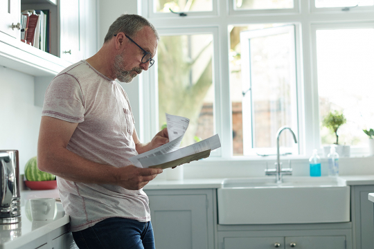 Man reading documents while standing in his kitchen.