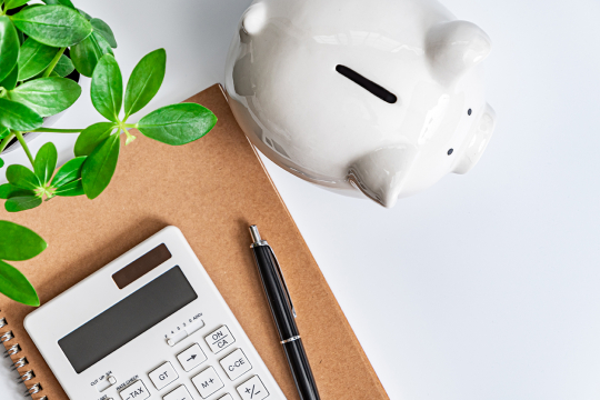 Piggy bank, calculator and notebook on a desk.