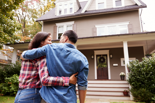 Couple looking at the front of their new home with their arms around each other.