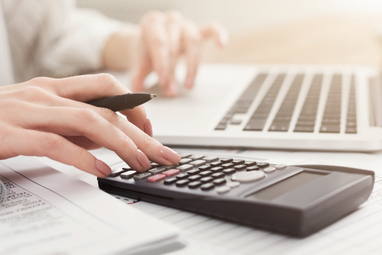 Close-up of a woman’s hands using a laptop and a calculator.