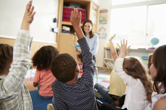 Young students with their hands raised.