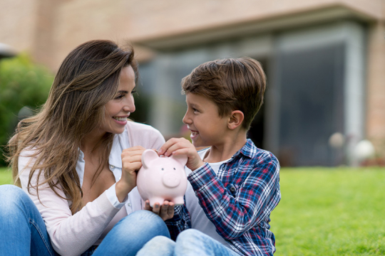 Mother and son putting coins into a piggy bank together.