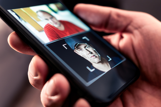 A hand holding a smartphone with the screen showing AI face-swapping software.