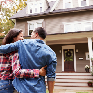 Un couple regardant la façade de leur maison en se tenant le bras.