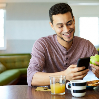 A smiling young man looking at his phone while eating lunch