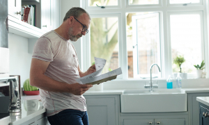 Man reading documents while standing in his kitchen.