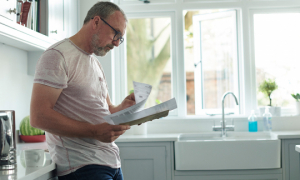 Un homme lisant des documents debout dans sa cuisine.